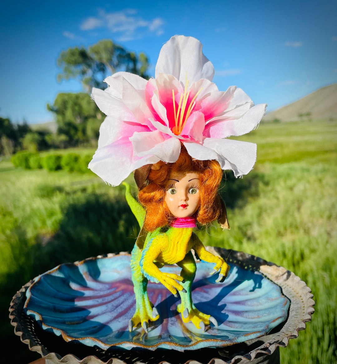 Vintage doll head with flower headdress on toy dinosaur body. 