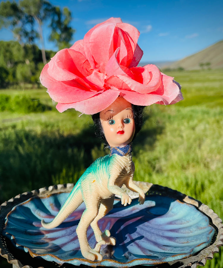 Vintage toy dinosaur body with vintage doll head and pink flower headdress. 5" tall, 3" long, 1 1/2" wide. 
