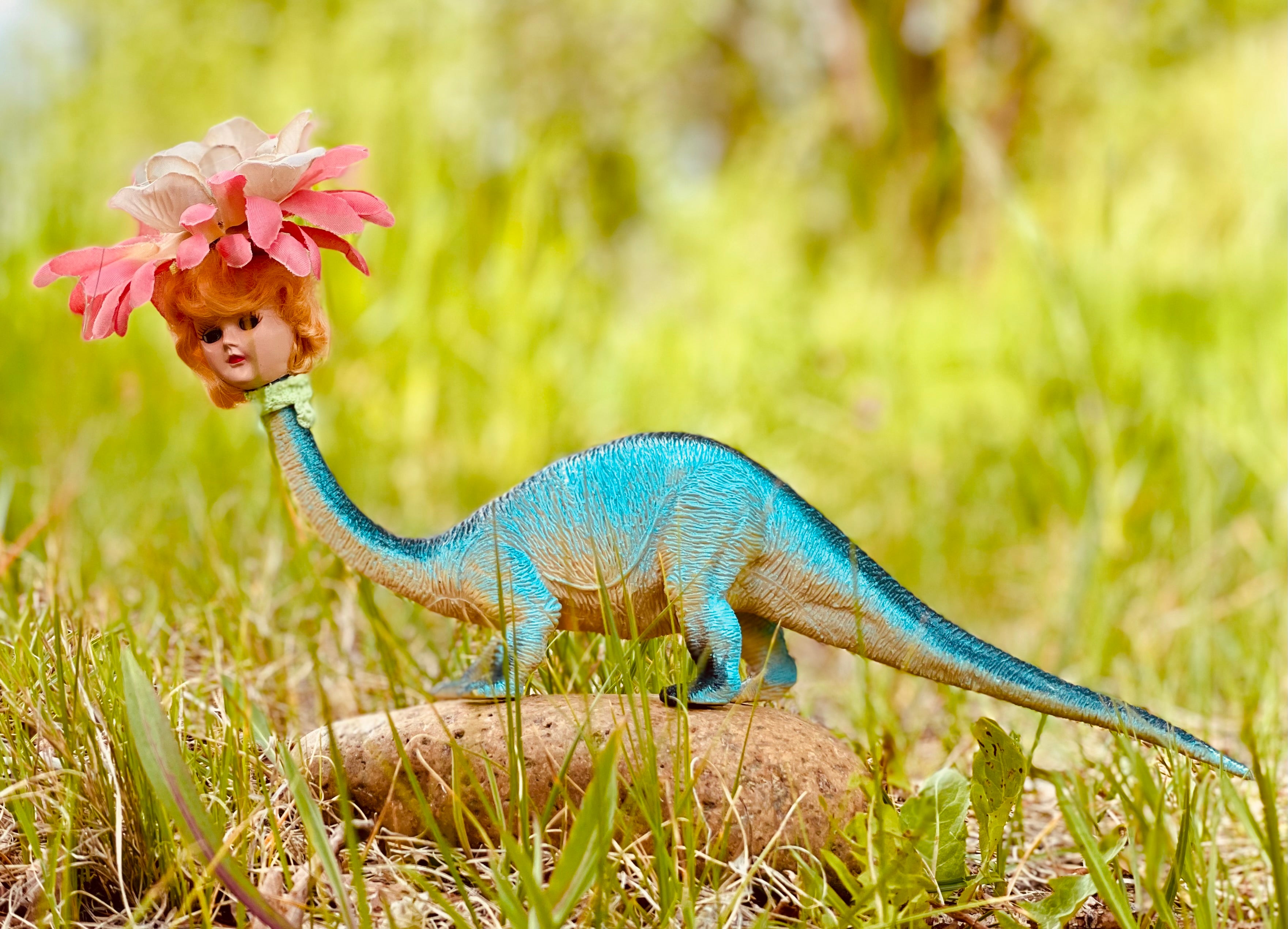 Vintage toy dinosaur with vintage doll head and flower headdress. 7" long , 5" tall, 2" wide. 