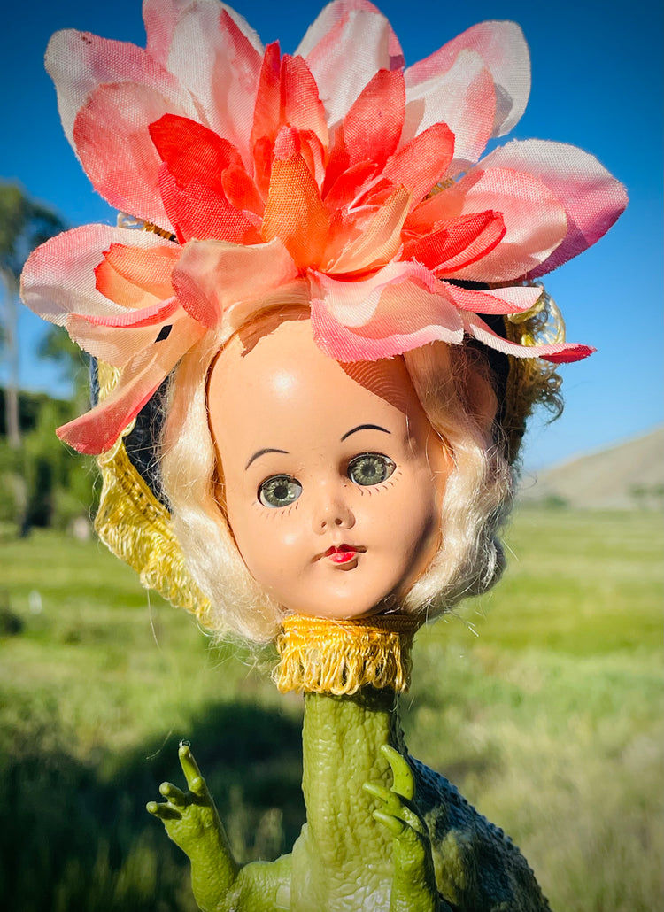 Close up of vintage doll head on a dinosaur body with a flower headdress