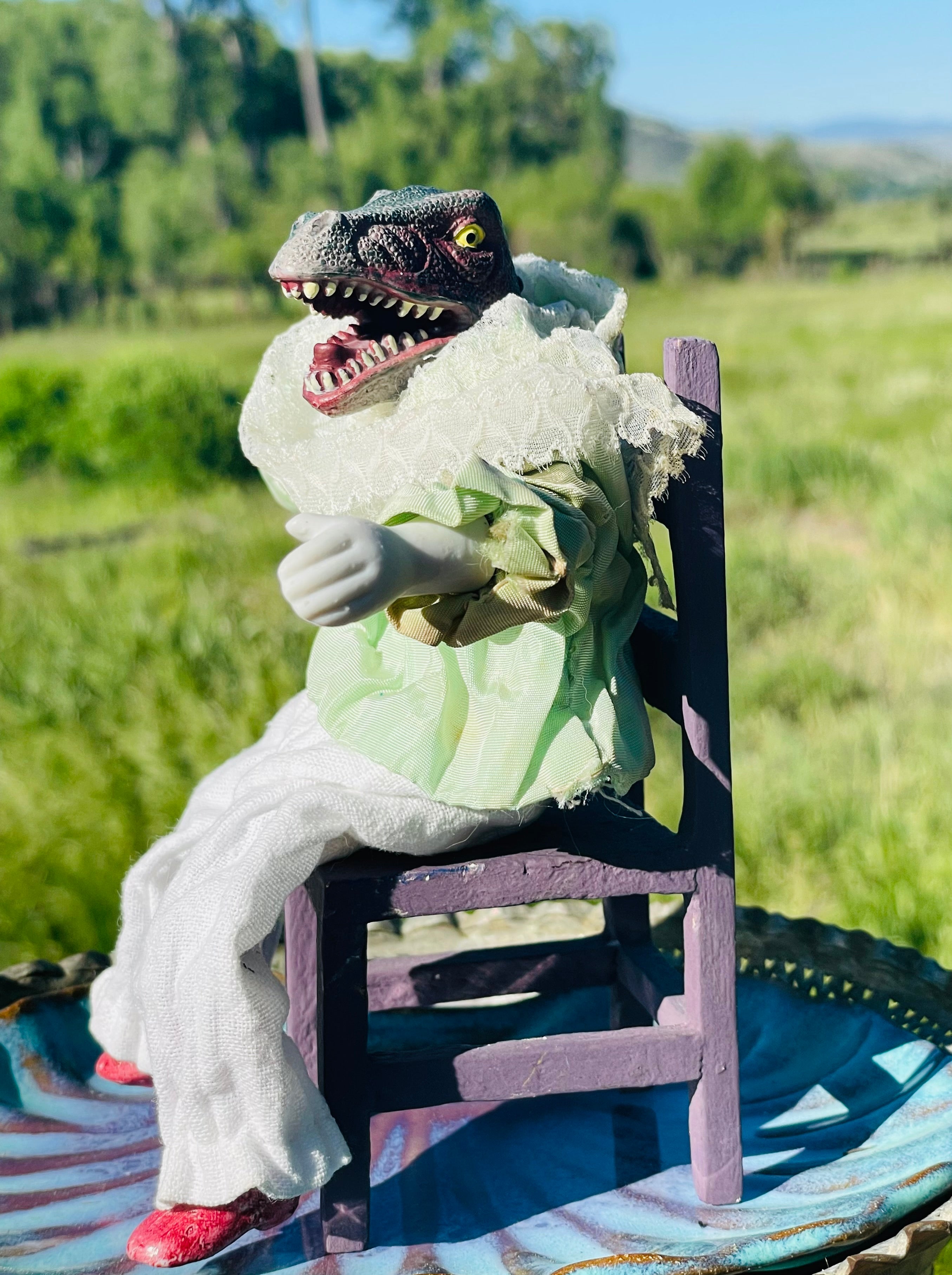 Posable doll with dinosaur head sitting on a tiny chair. 6" tall 