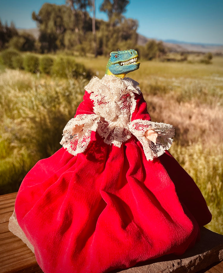 Dinosaur head on a vintage plastic doll in pleated red velvet dress with lace trim. 6"tall x 6" wide with skirt