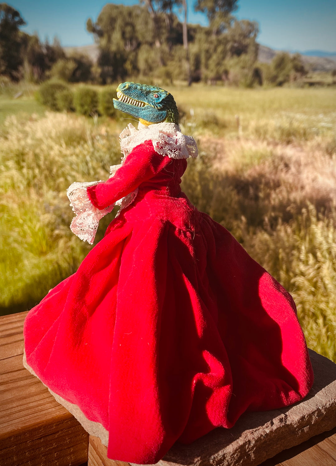 Sideview, Dinosaur head on a vintage plastic doll in pleated red velvet dress with lace trim. 6"tall x 6" wide with skirt