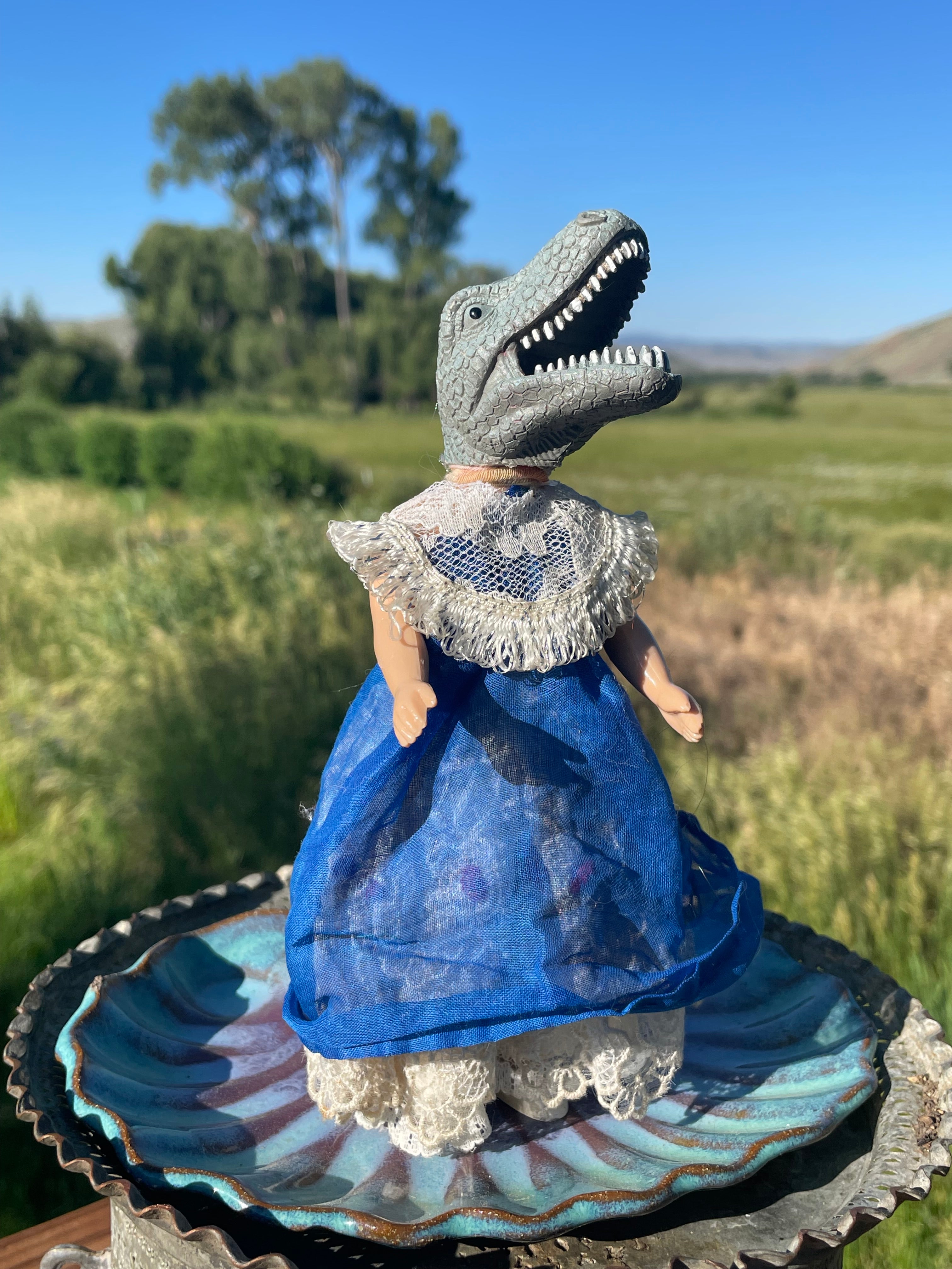 Vintage toy doll with a dinosaur head. Hand dyed blue gauze skirt over a lace pinafore with a lace bib collar. 6" tall x 3" wide.