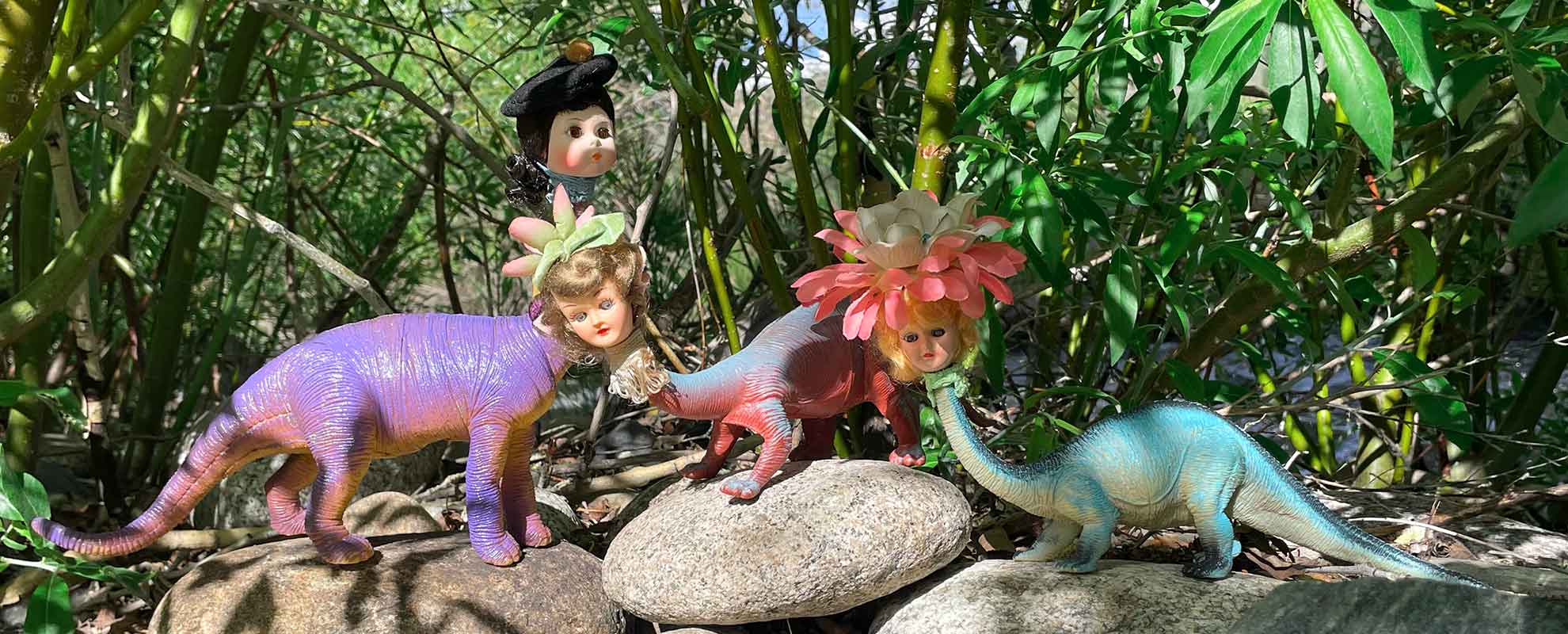 Three brontosaurs dolls with human heads wearing flowers as hats