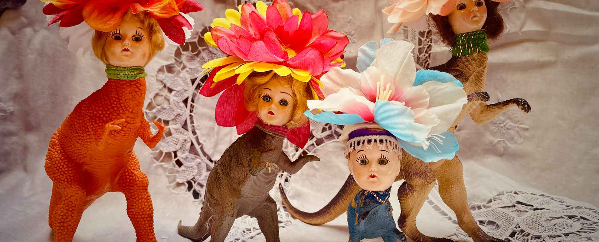 Four dinosaur human art dolls with human women heads with large flowers as hats and dinosaur bodies